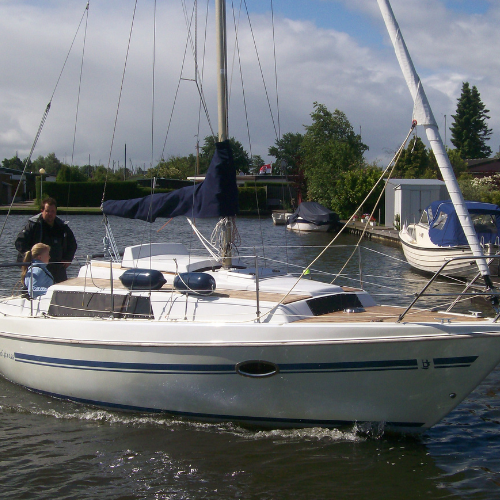 Segelboot Neptun 26 im Wasser. Das Segelboot hat eine einzigartige Perlmutt-Lackierung. Das Deck und die Plicht sind mit einem Teakholzbelag ausgestattet. Die aufgesetzten Fenster sind aus UV- beständigen Polycarbonat. Das Boot hat eine dunkelblaue Baumpersenning.